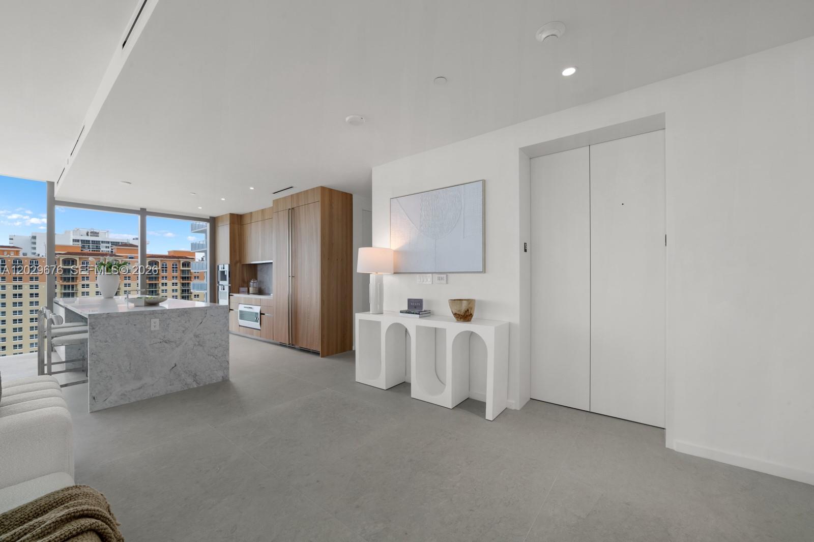 A modern kitchen with a marble island and wood cabinetry opens to a living area — 2000 S Ocean Dr # 15B, Hallandale Beach FL 33009, HALLANDALE BEACH, FL