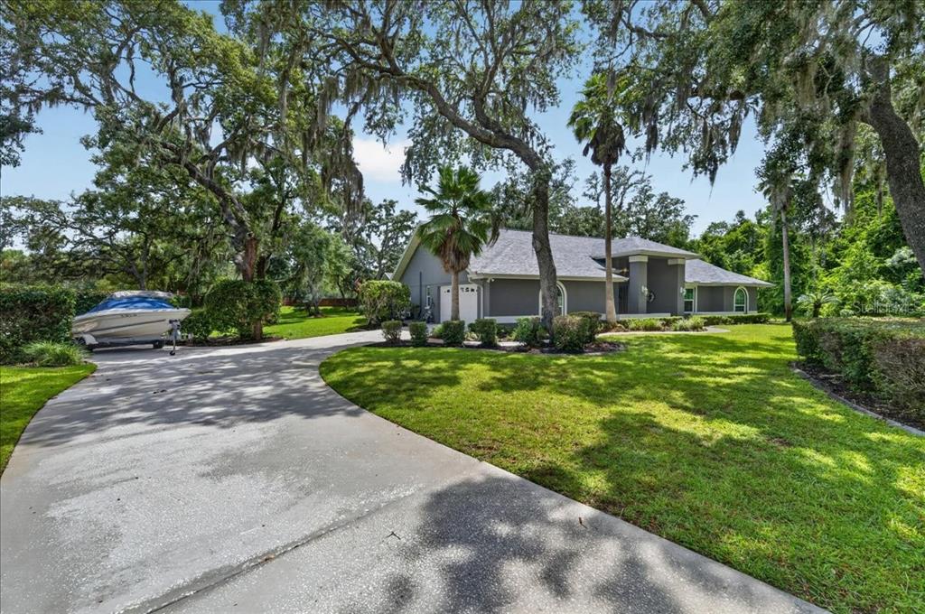 A gray single-story house with a concrete driveway, a boat on a trailer, and trees — 16754 CROSSBILL COURT, SPRING HILL, FL