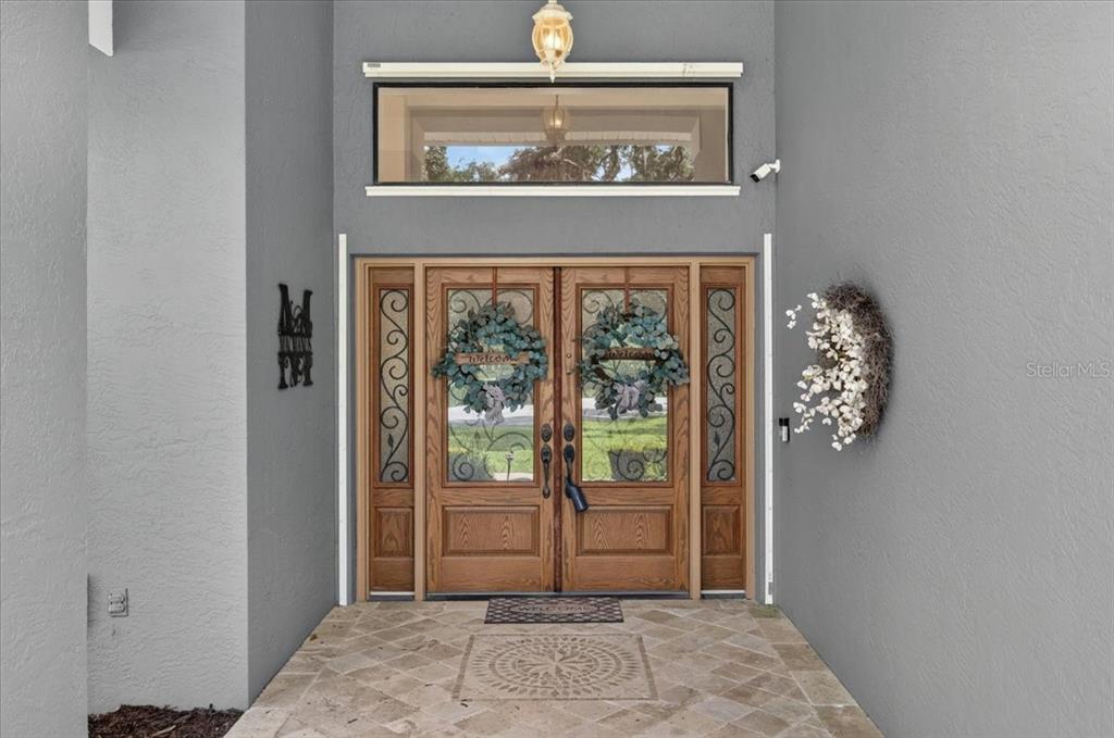 A front entryway features double wooden doors with glass panels and a rectangular transom window — 16754 CROSSBILL COURT, SPRING HILL, FL