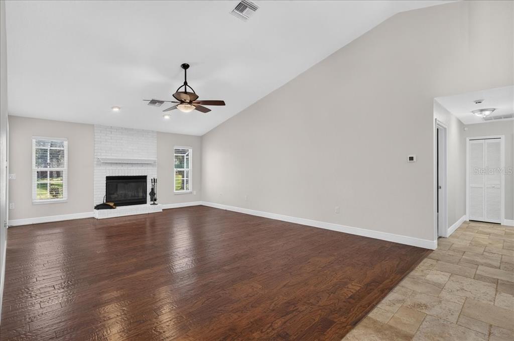 A living room with hardwood floors, a white brick fireplace, and a vaulted ceiling — 16754 CROSSBILL COURT, SPRING HILL, FL