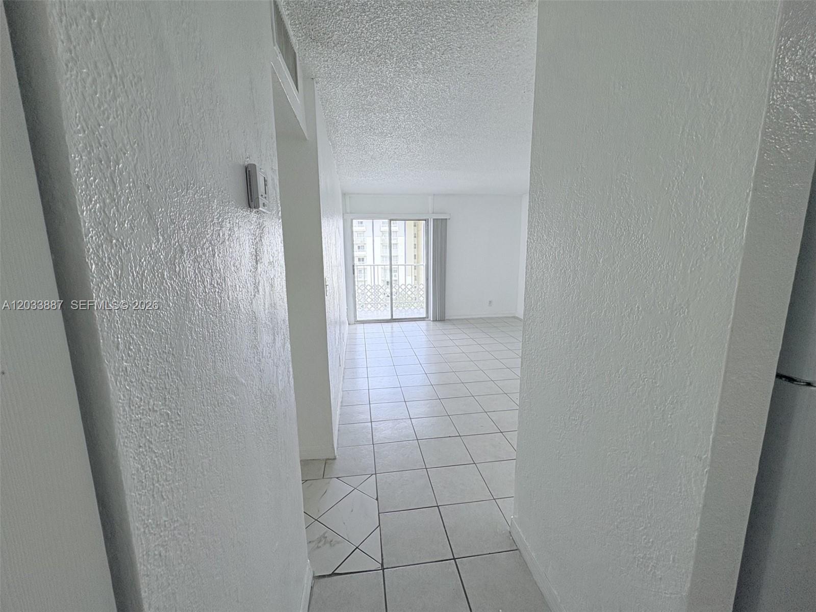 A white-walled hallway leads to an open living area with tiled floors and a balcony — 4550 NW 9th St # 717E, Miami FL 33126, MIAMI, FL