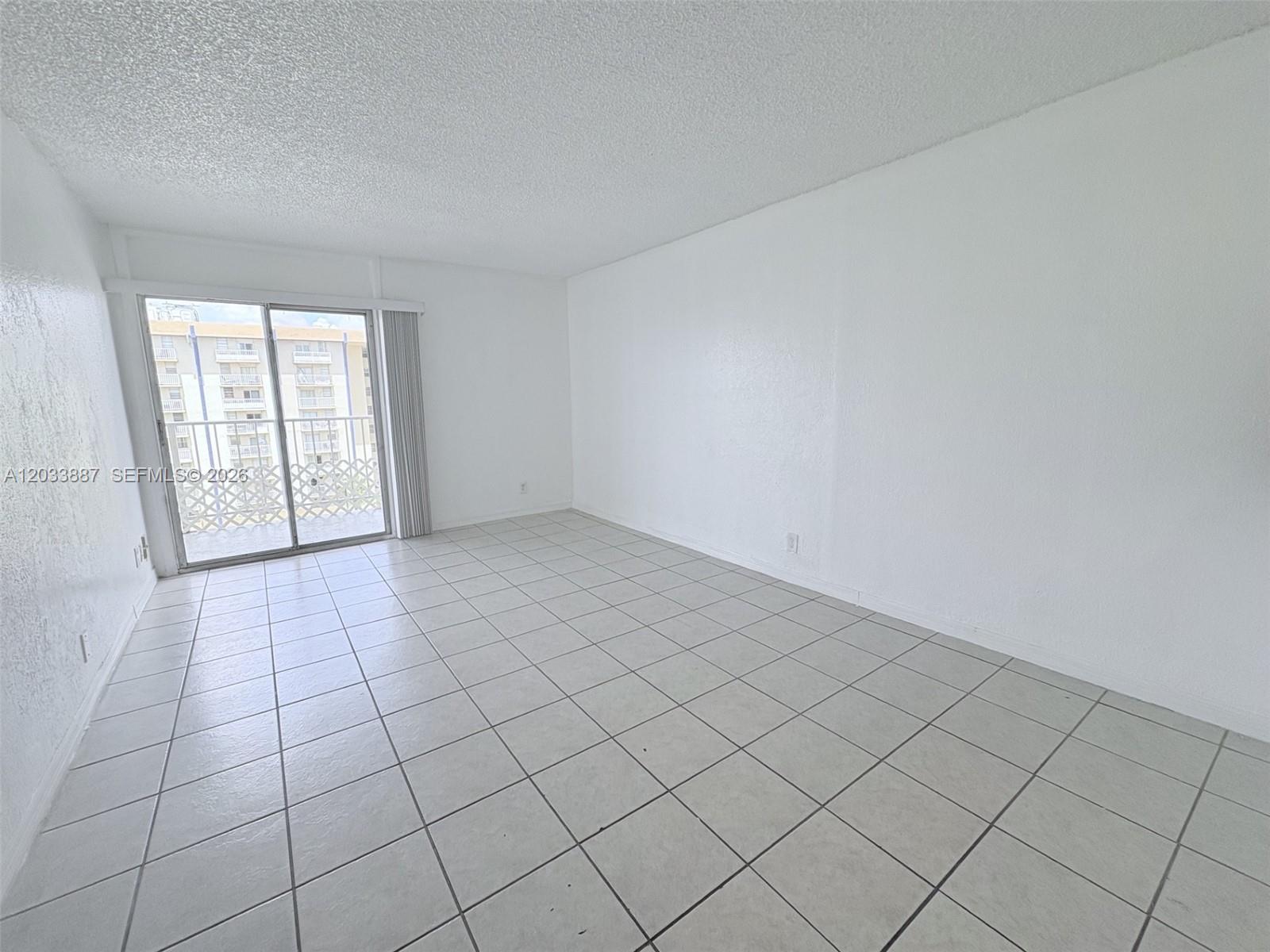 An empty room features white walls, light-colored tile flooring, and a sliding glass balcony door — 4550 NW 9th St # 717E, Miami FL 33126, MIAMI, FL