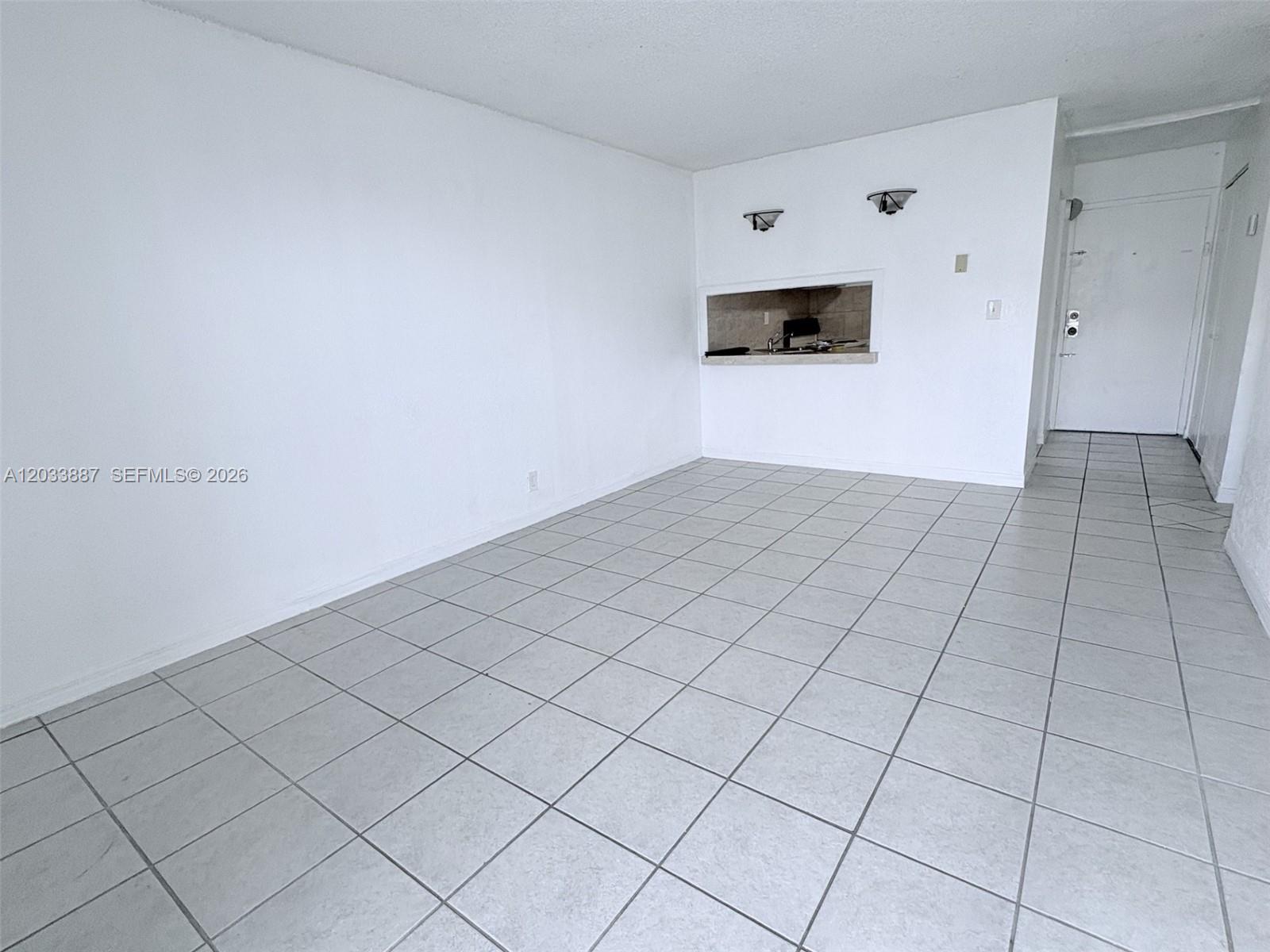 An empty room features white walls, light-colored square floor tiles, and a kitchen pass-through window — 4550 NW 9th St # 717E, Miami FL 33126, MIAMI, FL