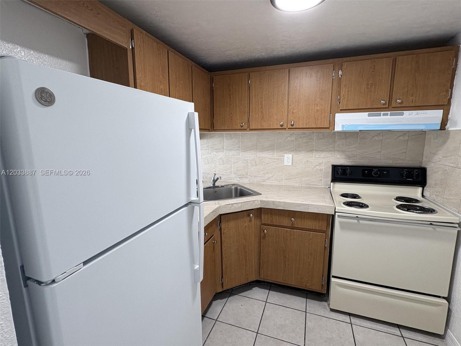 A kitchen features wood cabinets, a white refrigerator, a white stove, and tiled countertops — 4550 NW 9th St # 717E, Miami FL 33126, MIAMI, FL