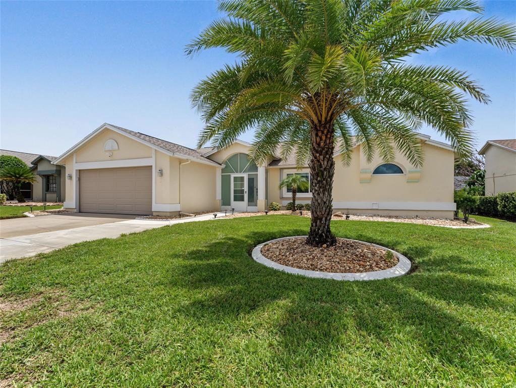 A single-story house with a beige exterior, a two-car garage, and a large palm tree — 8342 DANBURY LANE, HUDSON, FL