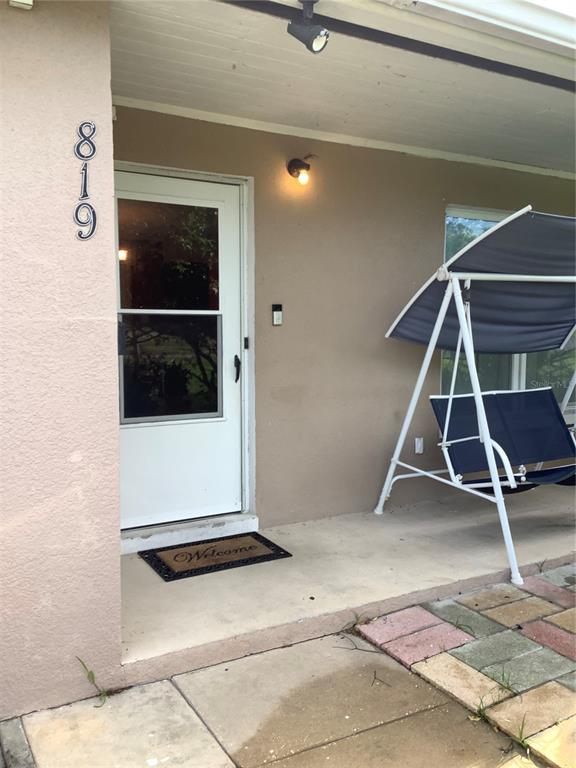 A covered porch features a white storm door, a welcome mat, and a patio swing — 819 62ND AVENUE S, ST PETERSBURG, FL