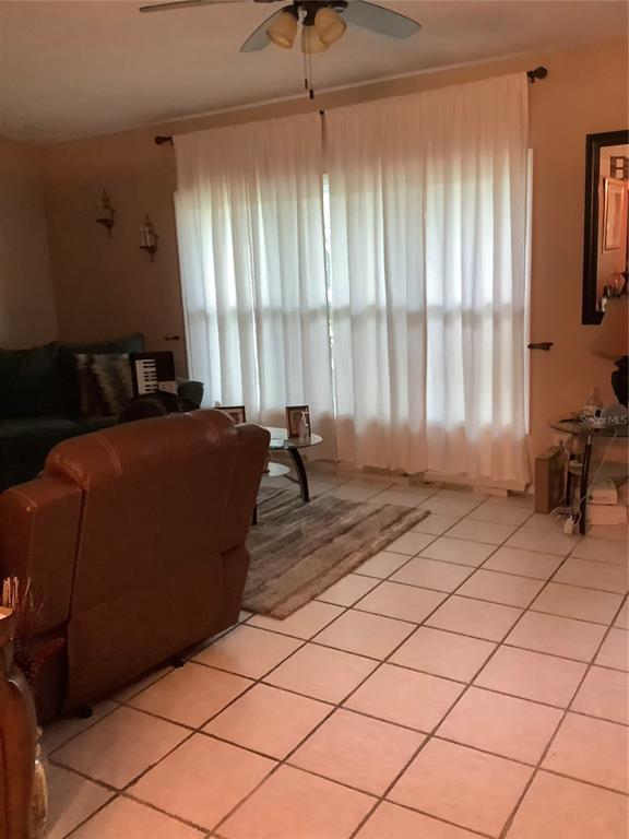 A living room features white floor-to-ceiling curtains, a brown leather recliner, and tiled flooring — 819 62ND AVENUE S, ST PETERSBURG, FL