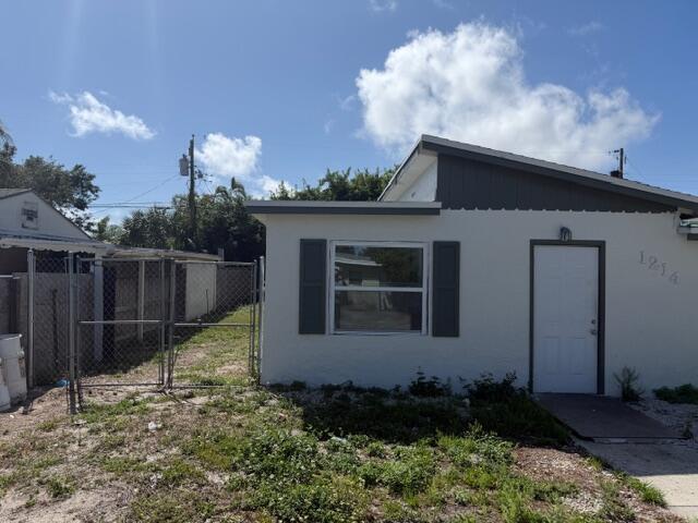 The exterior of a white, single-story house features a front door, window, and chain-link fence — 1214 Highview Road, Lake Worth FL 33462, LAKE WORTH, FL