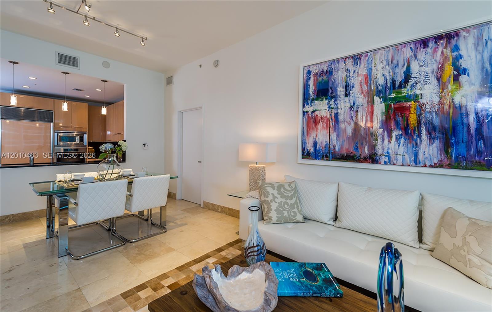 A modern living and dining area features white leather furniture, tile floors, and abstract art — 6799 Collins Ave # 503, Miami Beach FL 33141, MIAMI BEACH, FL
