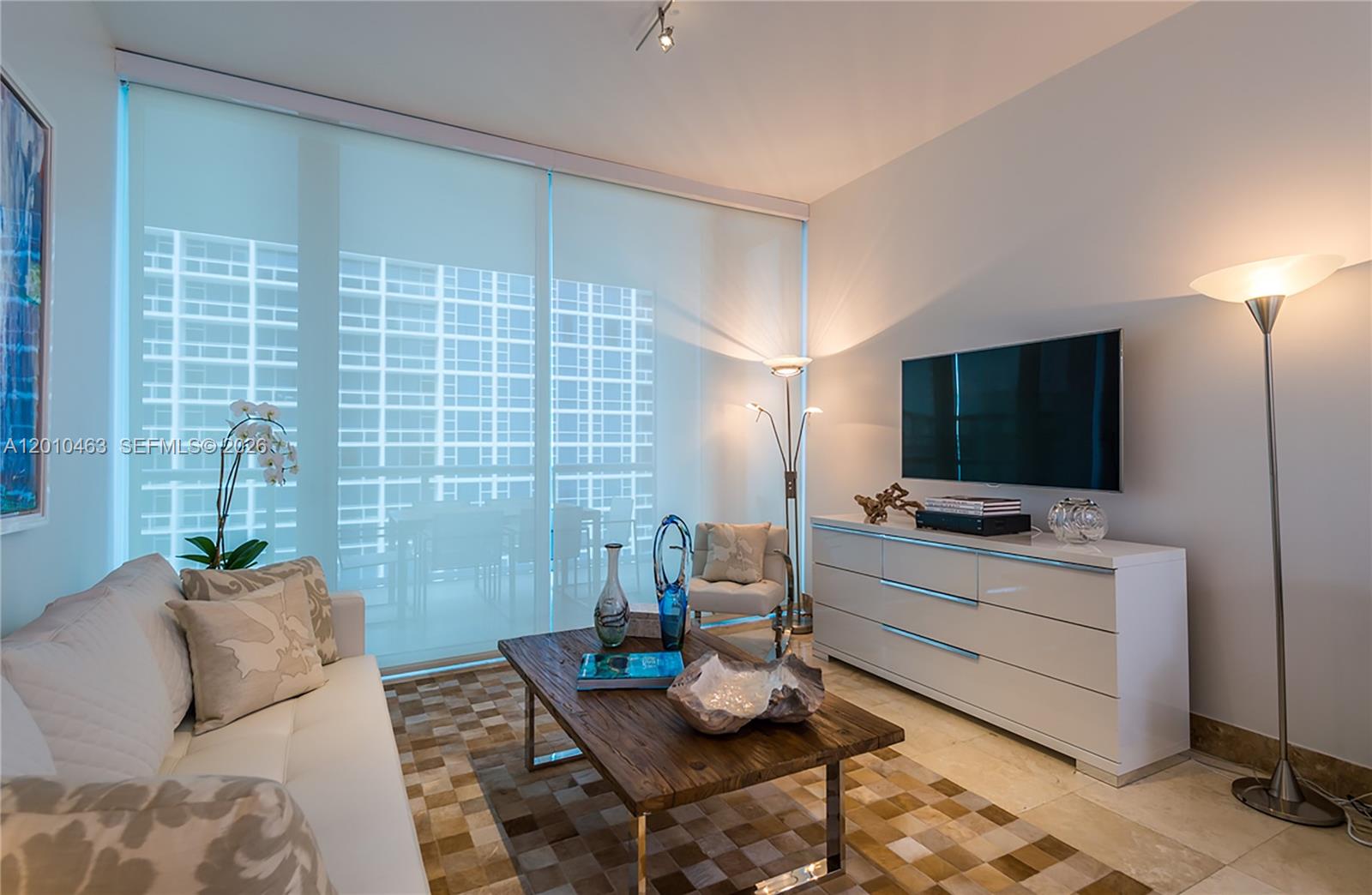 A modern living room features a white sofa, wooden coffee table, and a wall-mounted television — 6799 Collins Ave # 503, Miami Beach FL 33141, MIAMI BEACH, FL