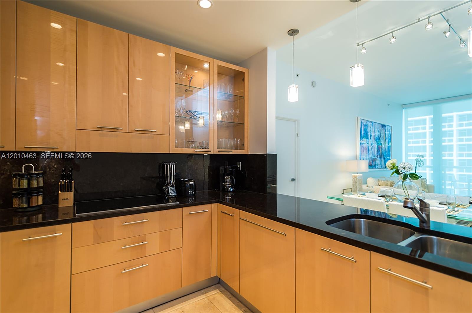 A kitchen features light wood cabinets, black countertops, and a stainless steel sink — 6799 Collins Ave # 503, Miami Beach FL 33141, MIAMI BEACH, FL