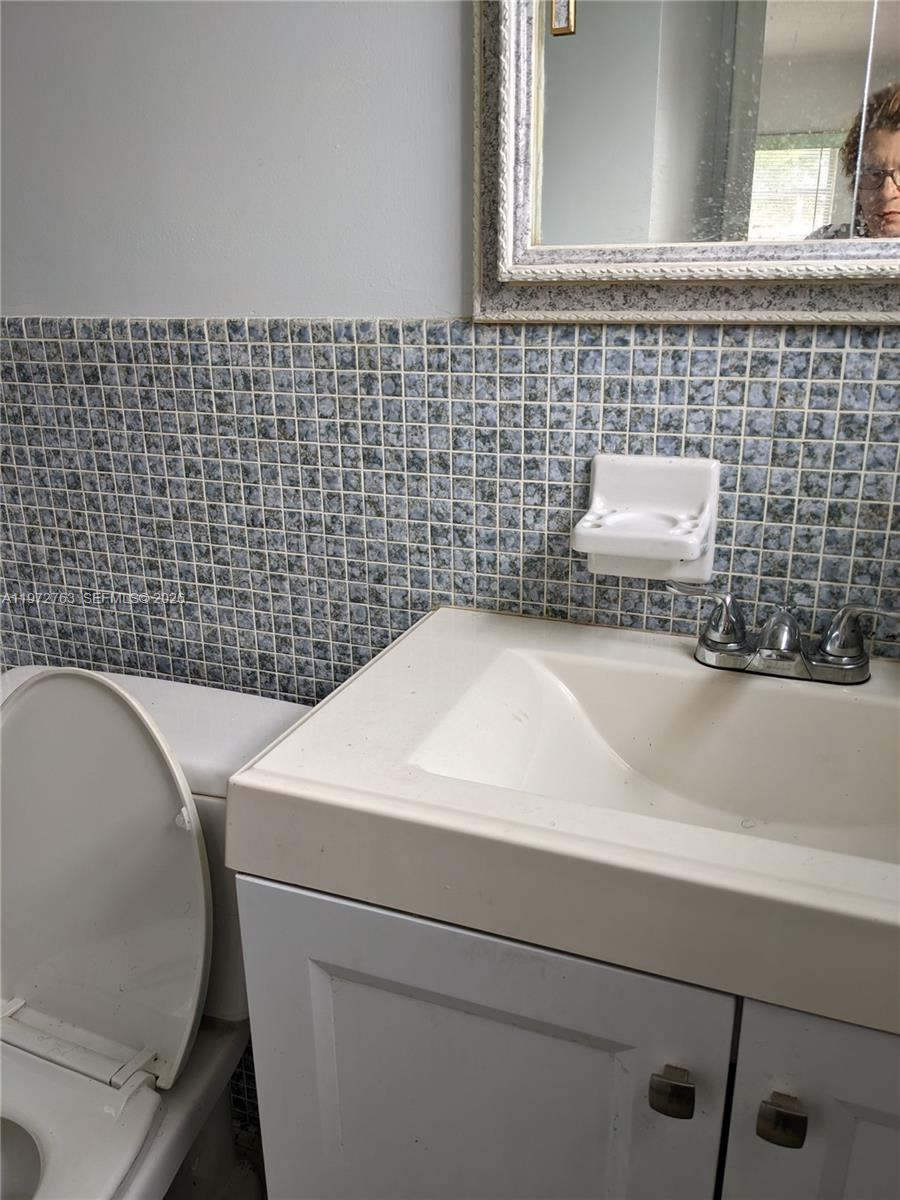 A bathroom features a white vanity, a toilet, and blue mosaic tile backsplash — 300 NE 191st St # 211, Miami FL 33179, MIAMI, FL
