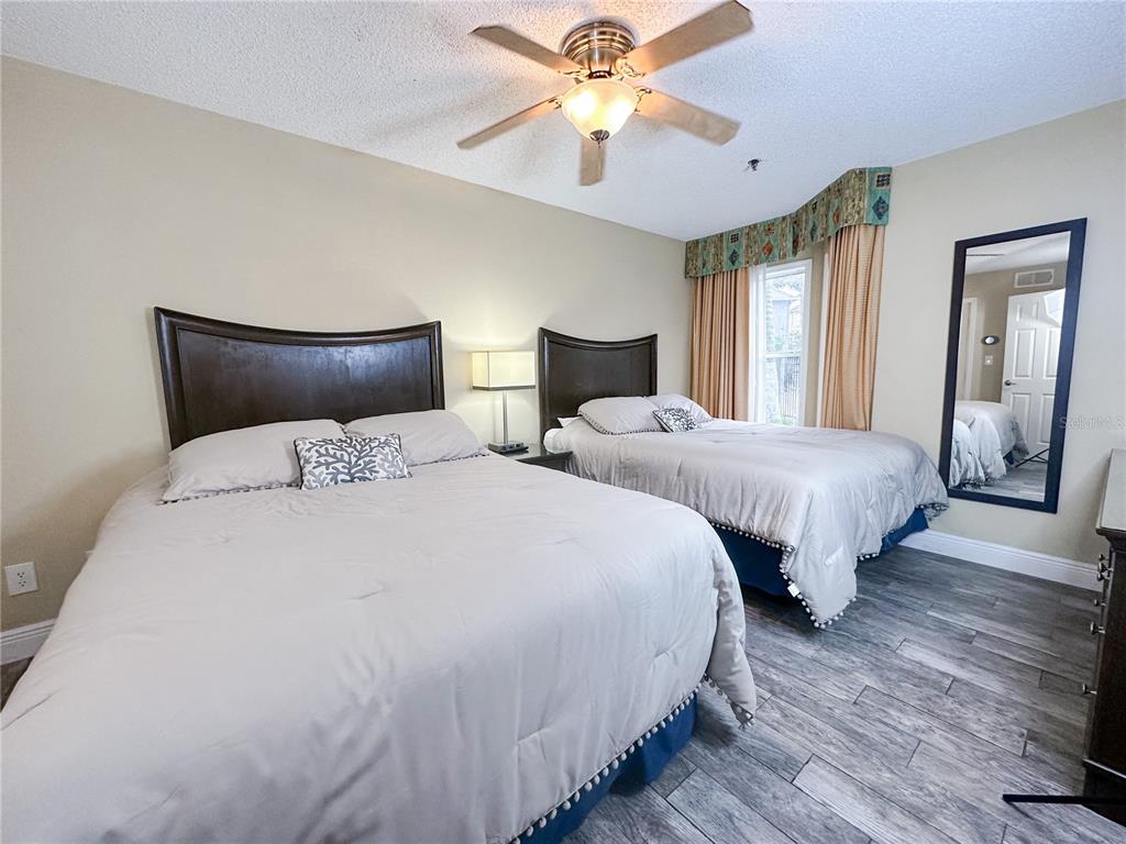 A bedroom features two beds, a ceiling fan, wood-look flooring, and a full-length mirror — 3100 PARKWAY BOULEVARD UNIT 110, KISSIMMEE, FL