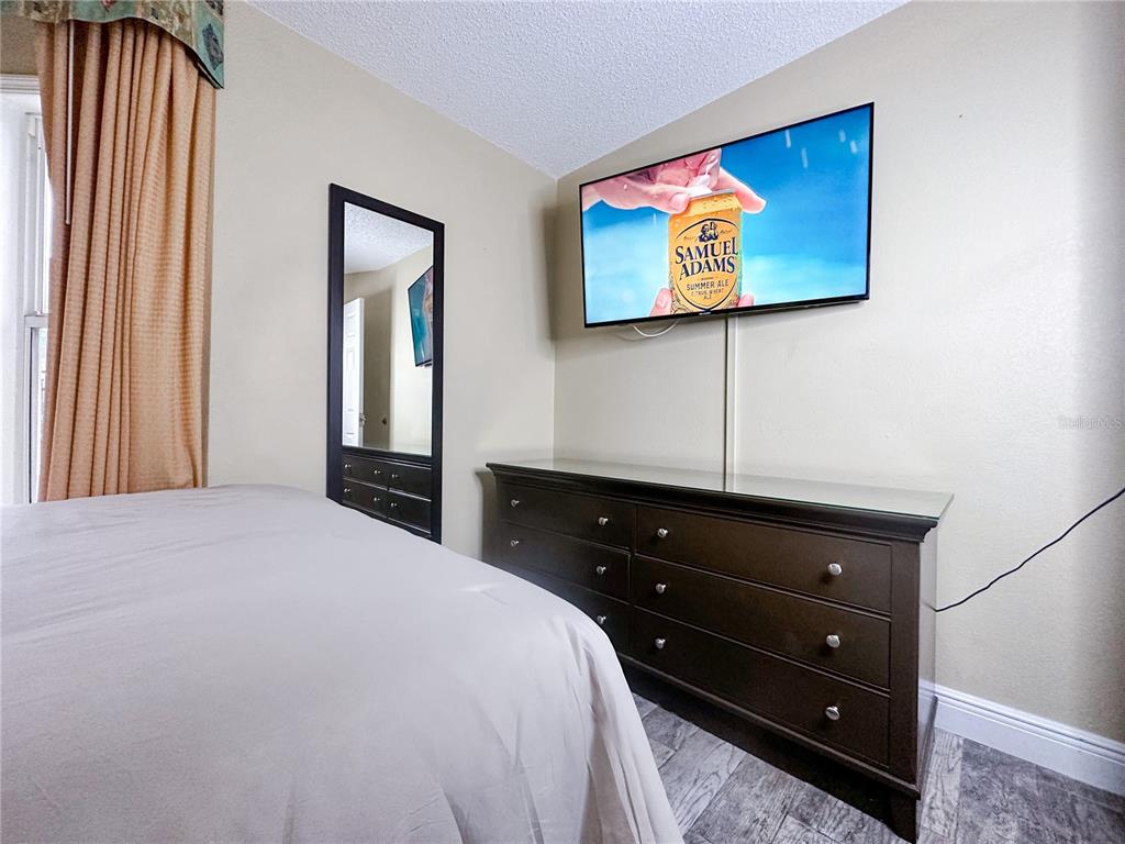 A bedroom features a bed, a dark wood dresser, a wall-mounted television, and a mirror — 3100 PARKWAY BOULEVARD UNIT 110, KISSIMMEE, FL