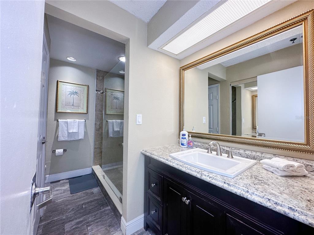 A bathroom features a dark wood vanity with a granite countertop and a large framed mirror — 3100 PARKWAY BOULEVARD UNIT 110, KISSIMMEE, FL