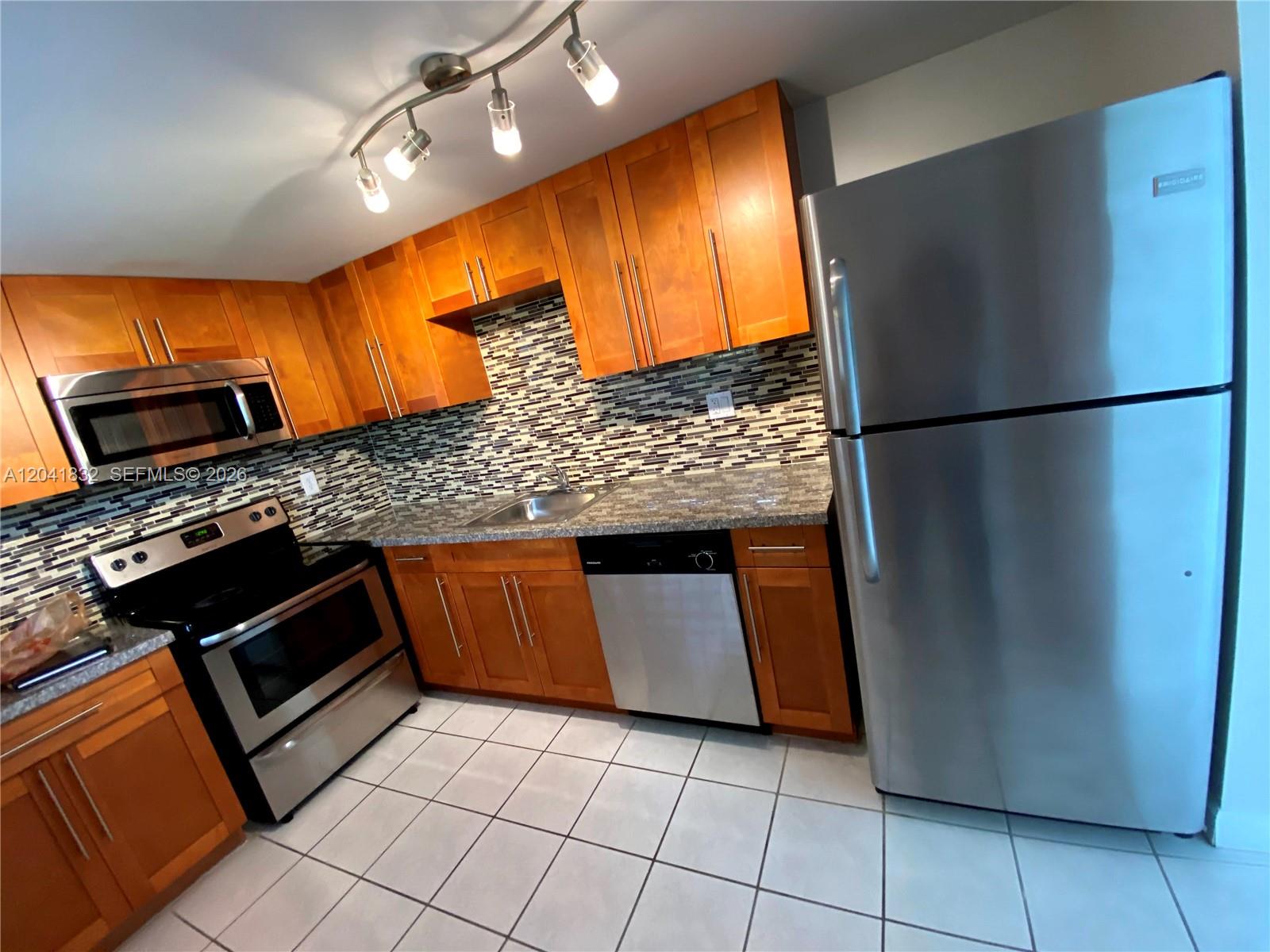 A kitchen features wood cabinets, stainless steel appliances, granite countertops, and a tiled backsplash — 9280 FONTAINEBLEAU BL # 103, Miami FL 33172, MIAMI, FL