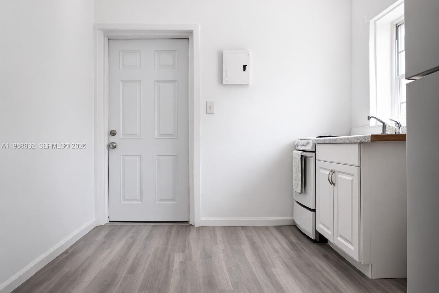A small kitchen features white cabinets, a white stove, and a door on a wood-look floor — 6250 NW Miami Pl # 2, Miami FL 33150, MIAMI, FL
