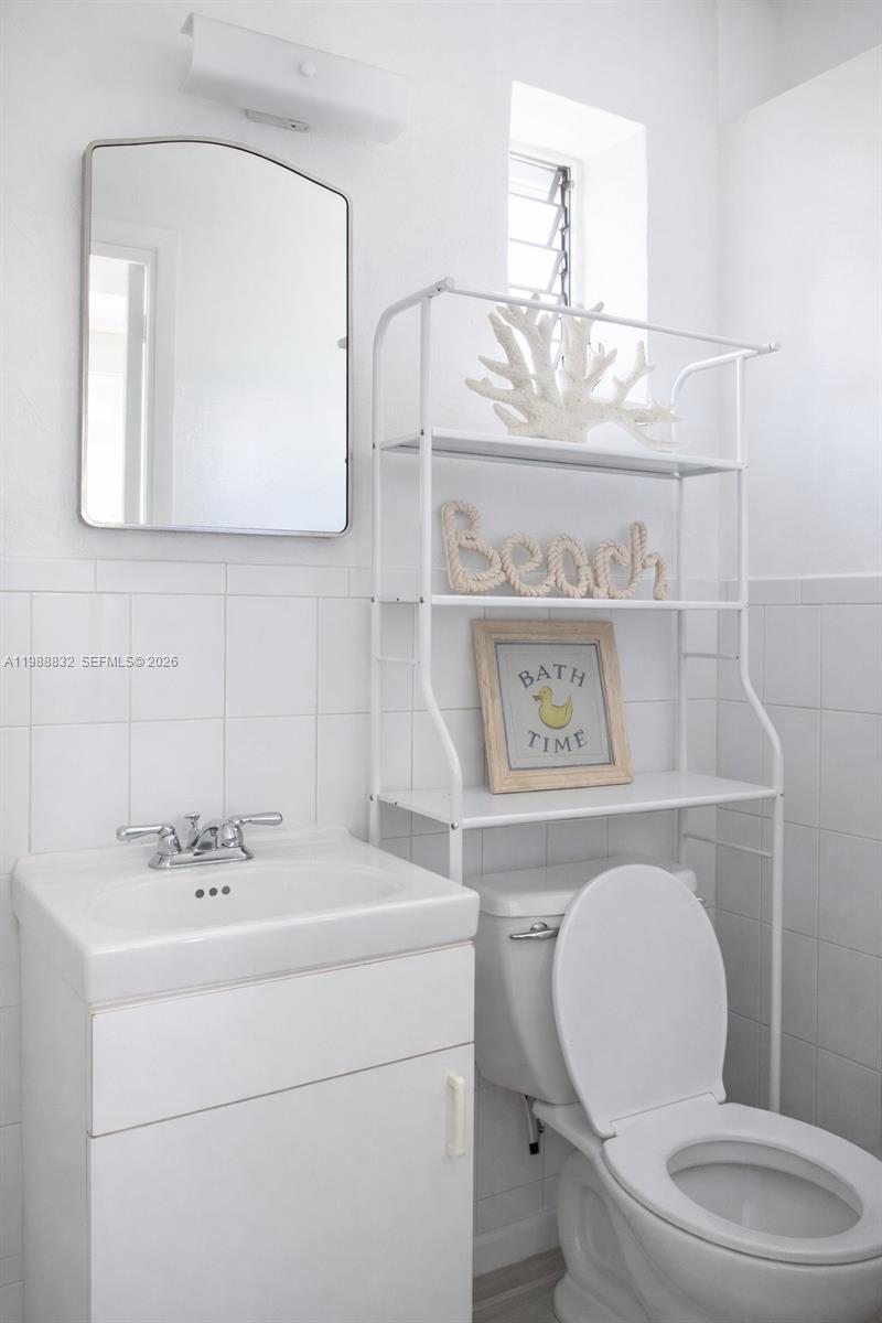 A white bathroom features a pedestal sink, a toilet, and a metal over-the-toilet storage unit — 6250 NW Miami Pl # 2, Miami FL 33150, MIAMI, FL