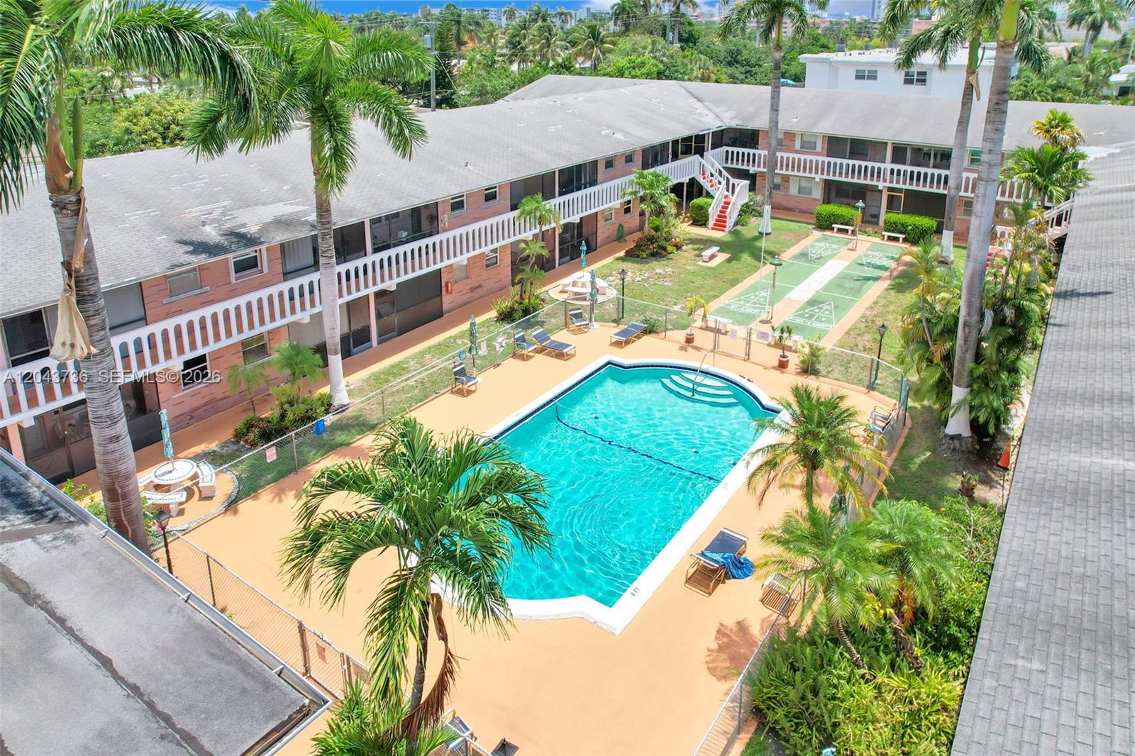 An aerial view shows an apartment complex courtyard with a swimming pool and shuffleboard courts — 160 NE 8th Ave # 27A, Hallandale Beach FL 33009, HALLANDALE BEACH, FL