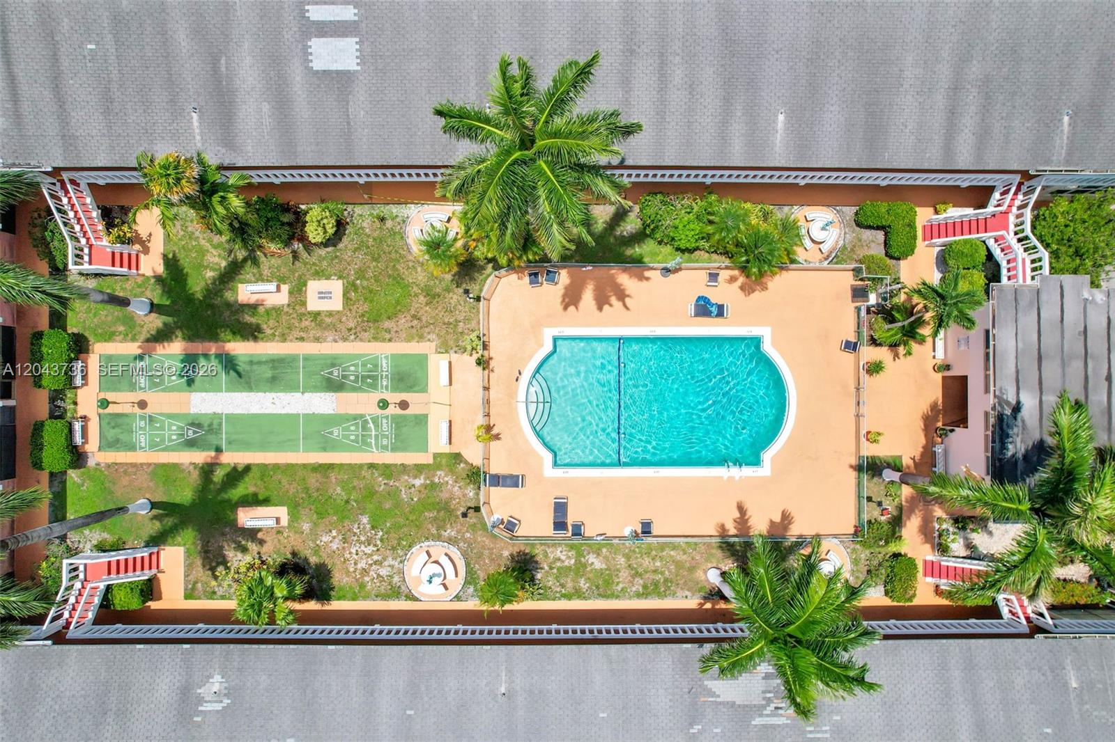 An aerial view shows a swimming pool, shuffleboard courts, and palm trees in a courtyard — 160 NE 8th Ave # 27A, Hallandale Beach FL 33009, HALLANDALE BEACH, FL