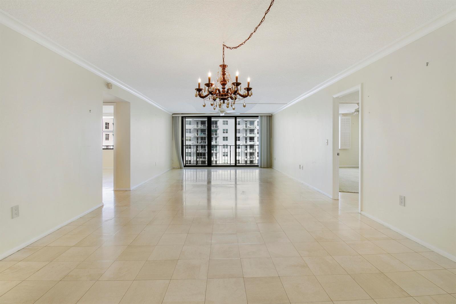 An empty, tiled living room features a crystal chandelier and a view of another building — 3456 S Ocean Boulevard # 6050, Palm Beach FL 33480, PALM BEACH, FL
