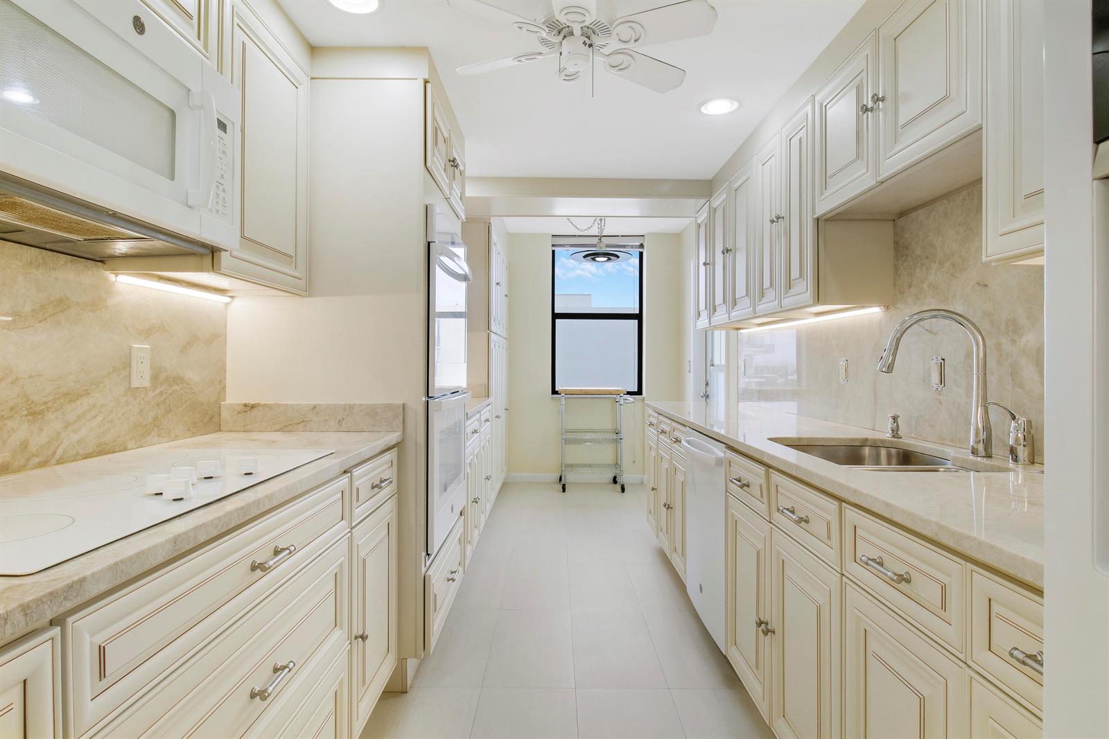 A galley kitchen features cream-colored cabinetry, marble countertops, stainless steel appliances, and a window — 3456 S Ocean Boulevard # 6050, Palm Beach FL 33480, PALM BEACH, FL