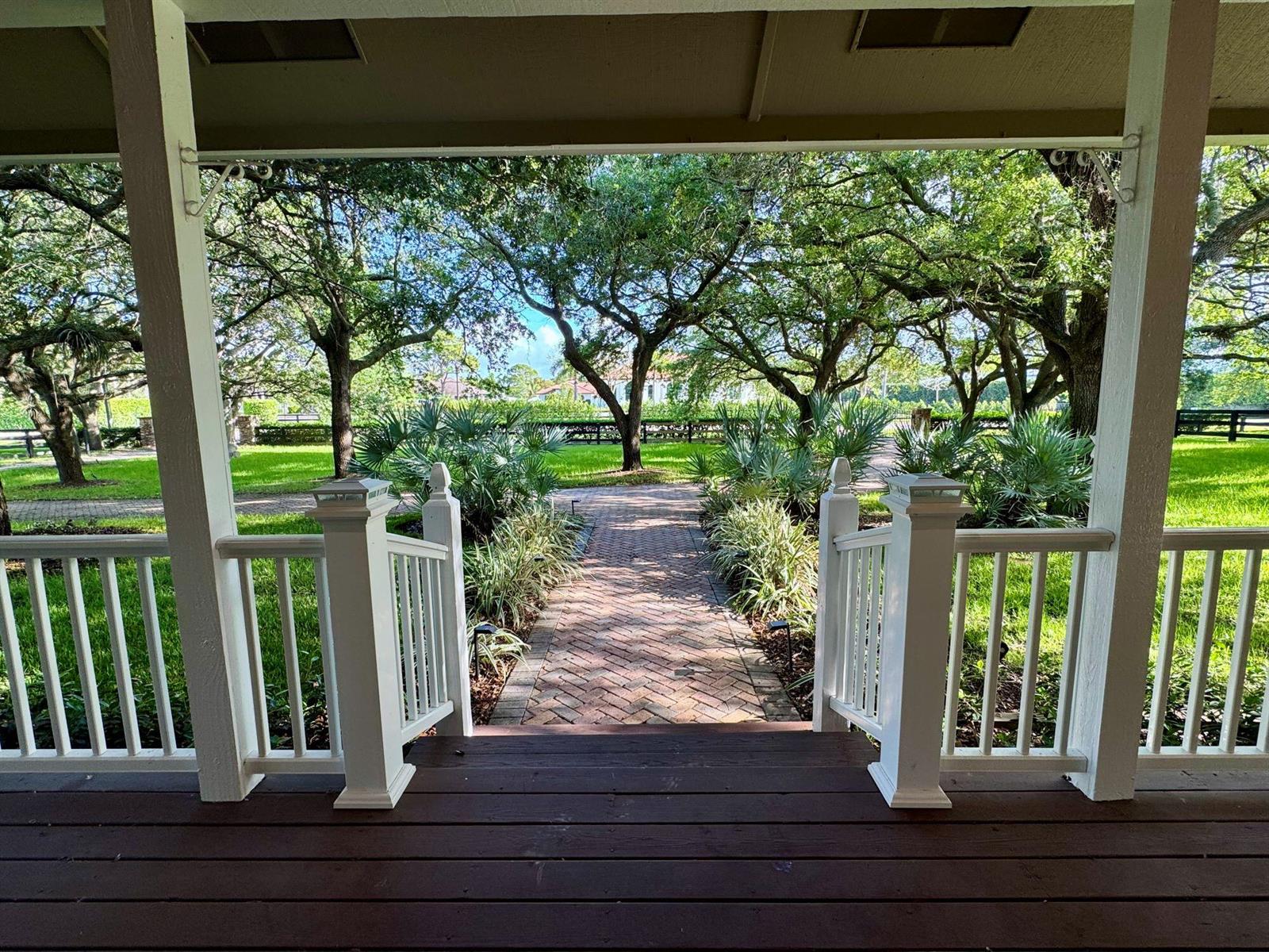 A view from a wooden porch looking out onto a brick walkway and lush trees — 14366 Belmont Trace, Wellington FL 33414, WELLINGTON, FL