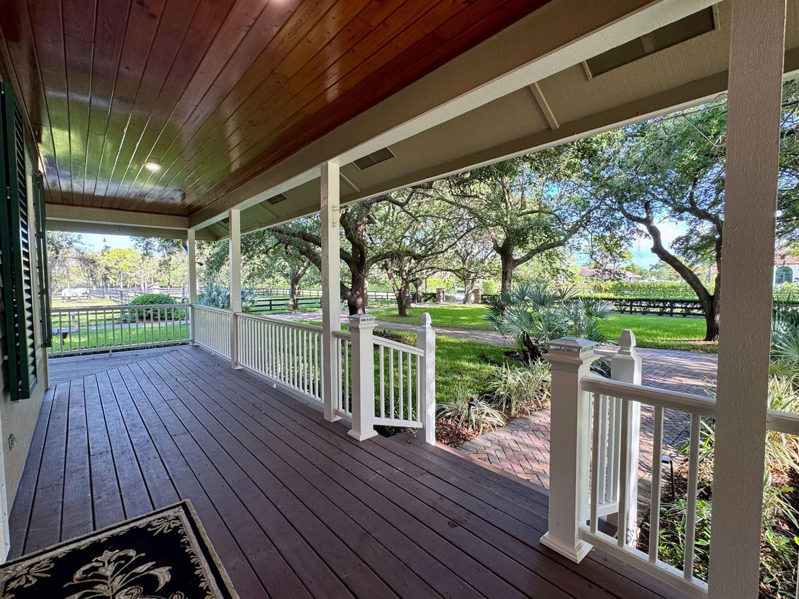 A covered wooden porch with white railings overlooks a grassy yard with mature trees — 14366 Belmont Trace, Wellington FL 33414, WELLINGTON, FL
