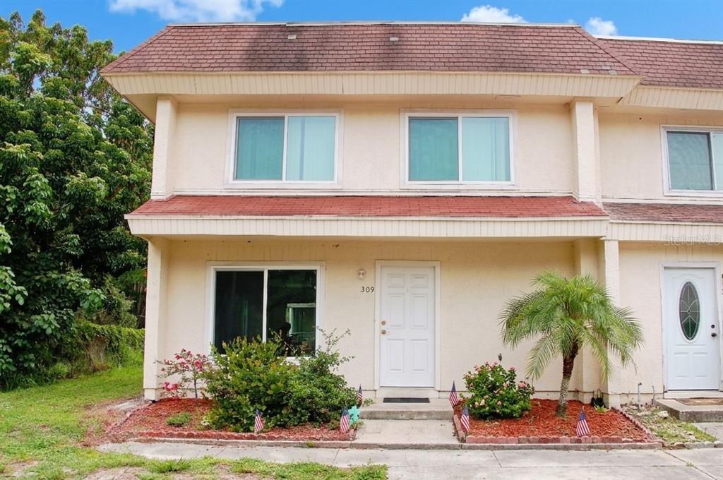 A two-story townhouse exterior features beige stucco walls, a red shingled roof, and small gardens — 309 AMHERST AVENUE UNIT 51, SARASOTA, FL