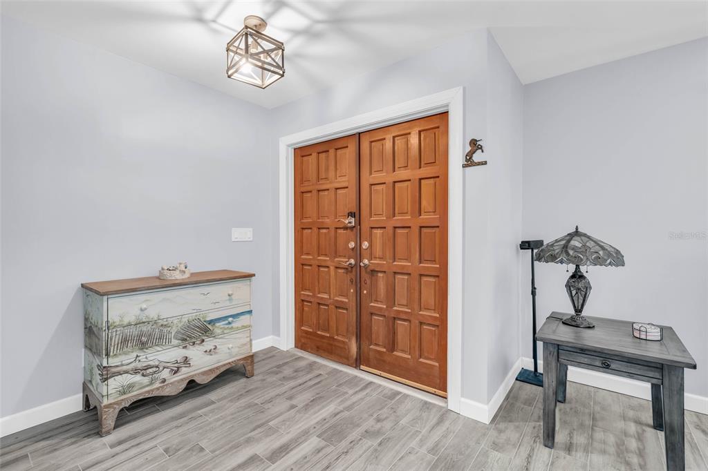 An entryway features double wooden doors, gray wood-look tile flooring, and a decorative light fixture — 4636 BUCK KEY ROAD, SANIBEL, FL