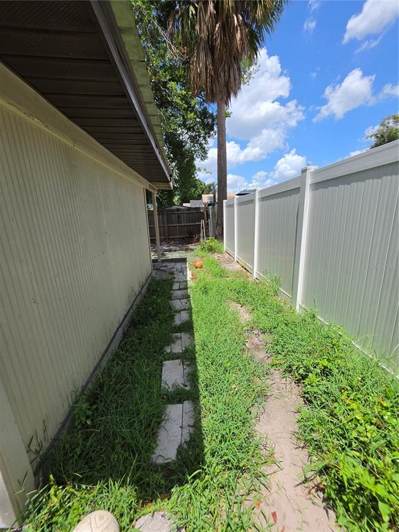 A narrow side yard features a stone path, overgrown grass, and a white vinyl fence — 3308 E MOHAWK AVE, TAMPA, FL