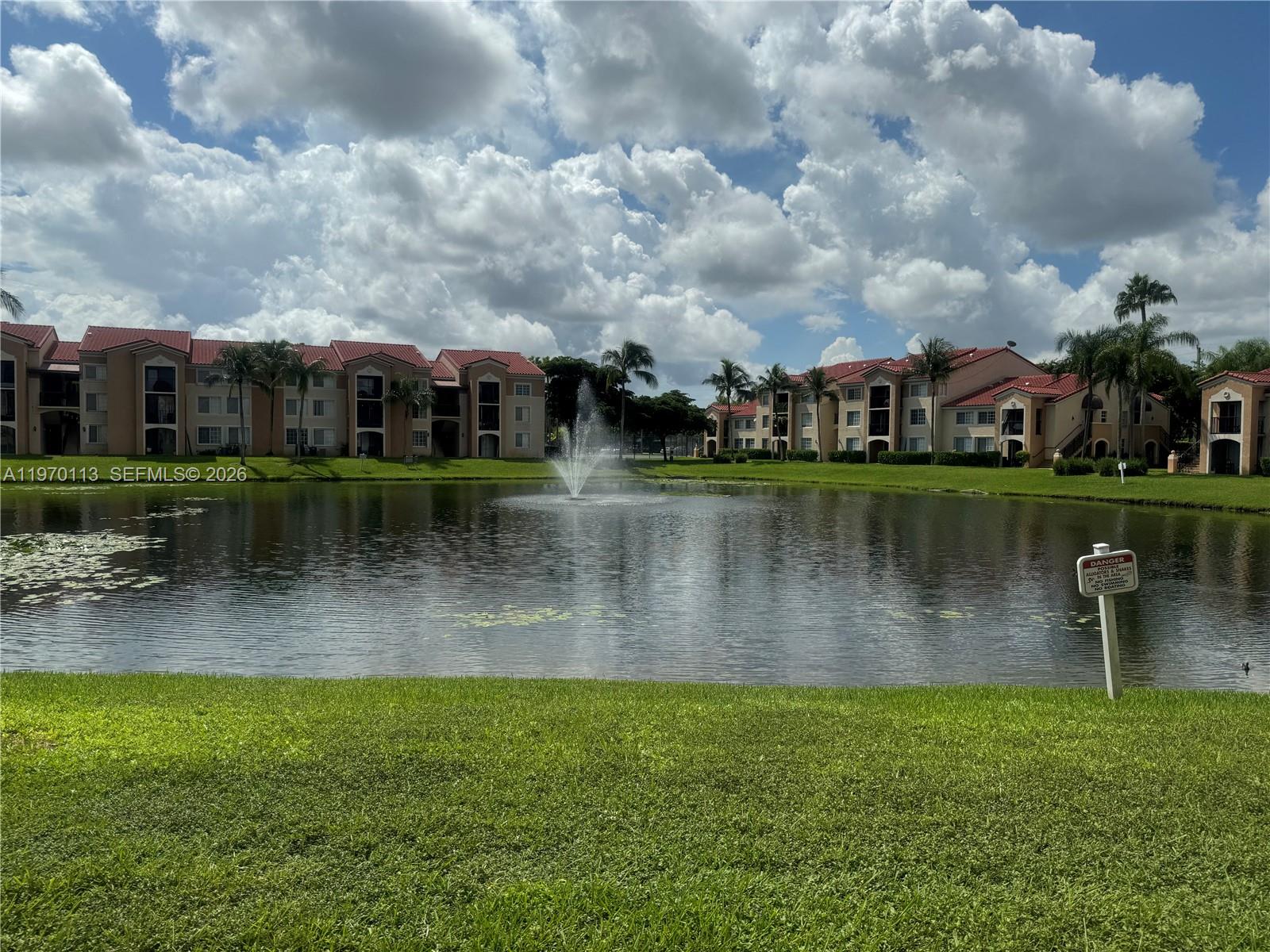 A pond with a fountain sits in front of multi-story apartment buildings under a cloudy sky — 2091 Renaissance Blvd # 104, Miramar FL 33025, MIRAMAR, FL