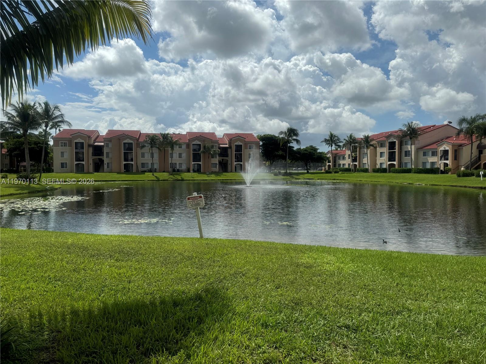 A pond with a fountain sits in front of multi-story apartment buildings under a cloudy sky — 2091 Renaissance Blvd # 104, Miramar FL 33025, MIRAMAR, FL