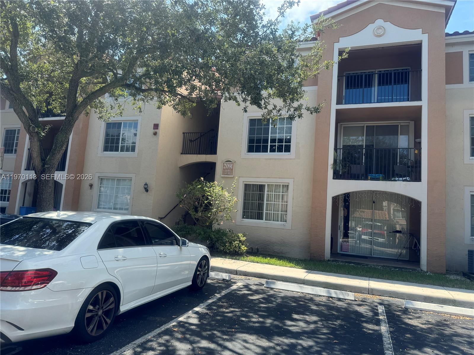 A white sedan is parked in front of a three-story tan apartment building — 2091 Renaissance Blvd # 104, Miramar FL 33025, MIRAMAR, FL