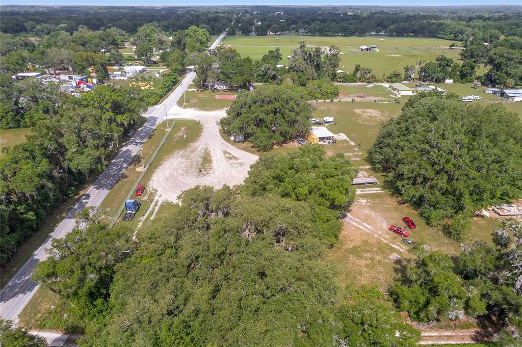 An aerial view shows a rural property with large trees, a gravel driveway, and vehicles — 1751 E HIGHWAY 329, CITRA, FL