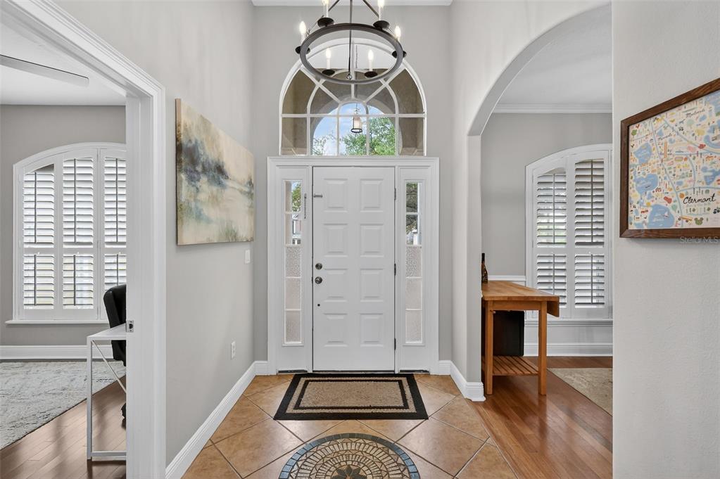 A bright foyer features tile flooring, a white front door, and a circular chandelier — 1245 SHORECREST CIR, CLERMONT, FL