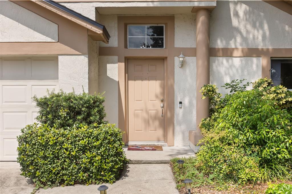 The exterior of a home features a tan front door, a transom window, and landscaping — 4562 CONWAY LANDING DRIVE, ORLANDO, FL