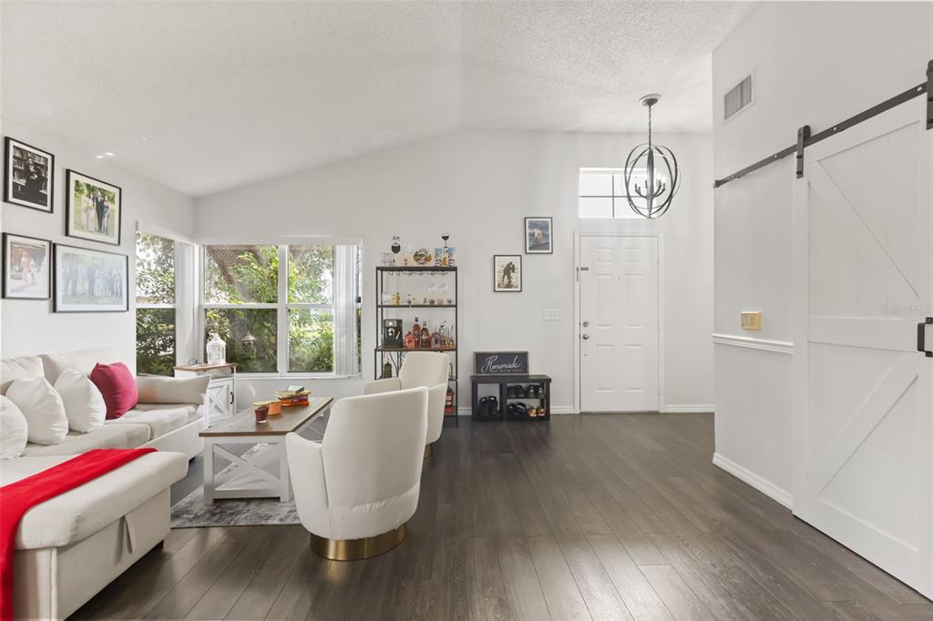 A living room features white walls, dark wood flooring, a vaulted ceiling, and a sliding barn door — 4562 CONWAY LANDING DRIVE, ORLANDO, FL