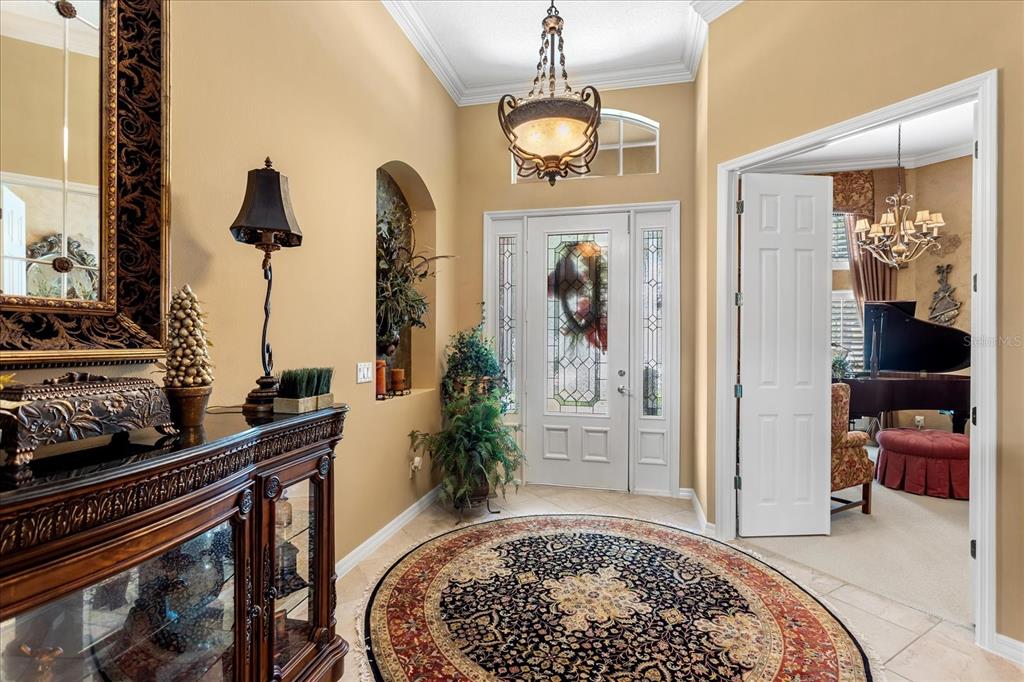 A foyer features a circular rug, a chandelier, a decorative mirror, and a grand piano — 131 ALEXANDRIA PLACE DRIVE, APOPKA, FL