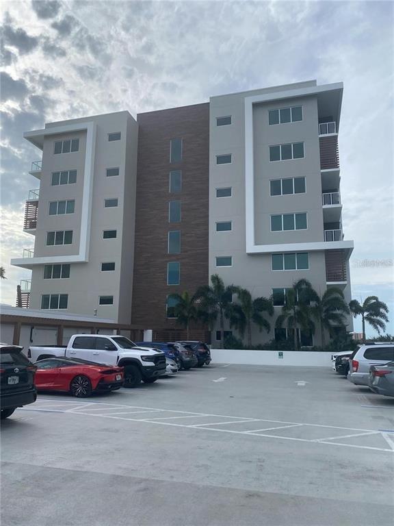 A modern multi-story apartment building stands behind a paved parking lot with several parked vehicles — 920 N OSCEOLA AVENUE UNIT 405, CLEARWATER, FL