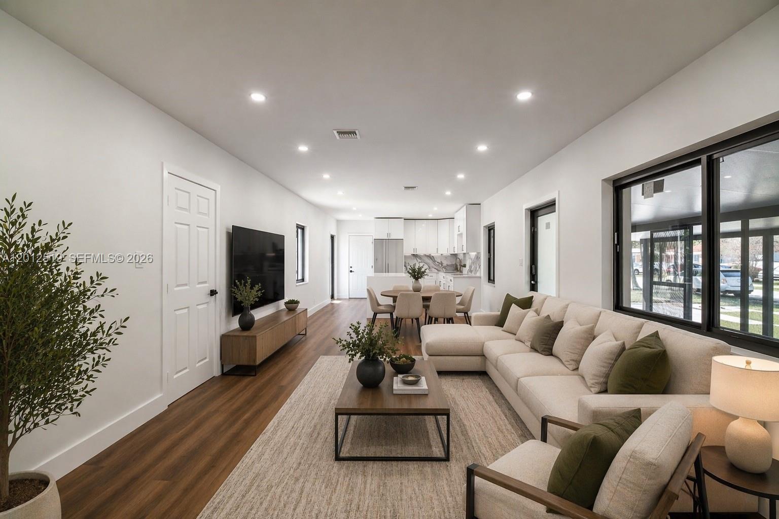 An open-concept living room and kitchen feature white walls, wood flooring, and modern neutral furniture — 220 NW 144th St, Miami FL 33168, MIAMI, FL