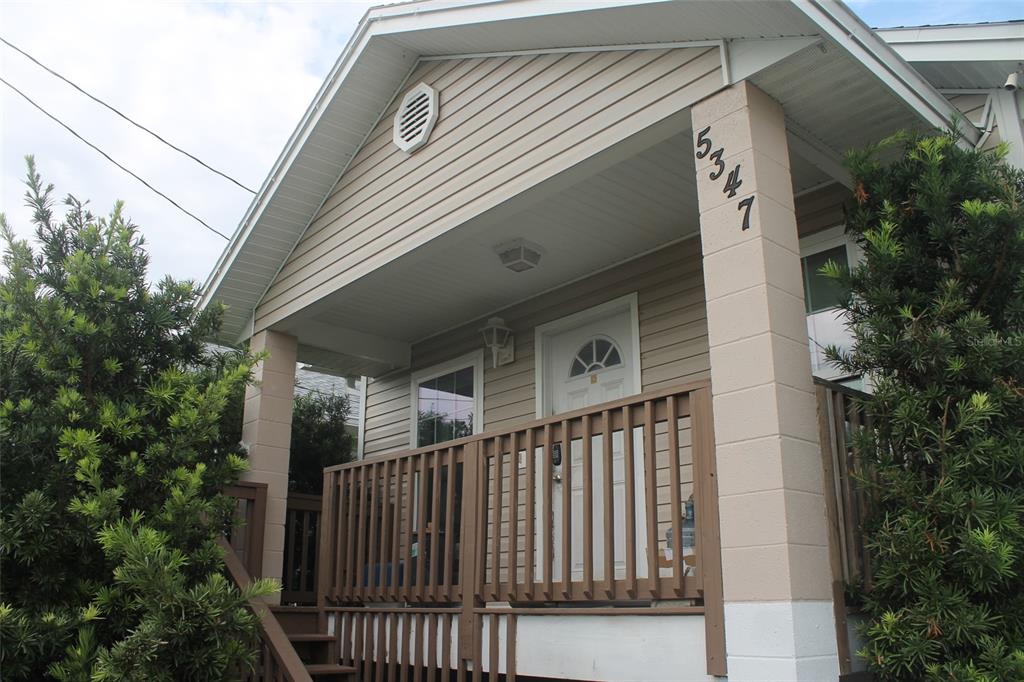 A tan house exterior features a covered front porch with wooden railings and concrete pillars — 5347 LEISURE LN, NEW PORT RICHEY, FL