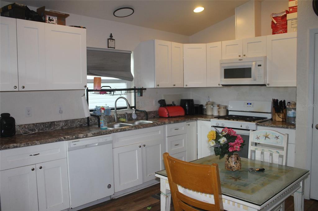 A kitchen with white cabinets, granite countertops, a dishwasher, and a dining table — 5347 LEISURE LN, NEW PORT RICHEY, FL