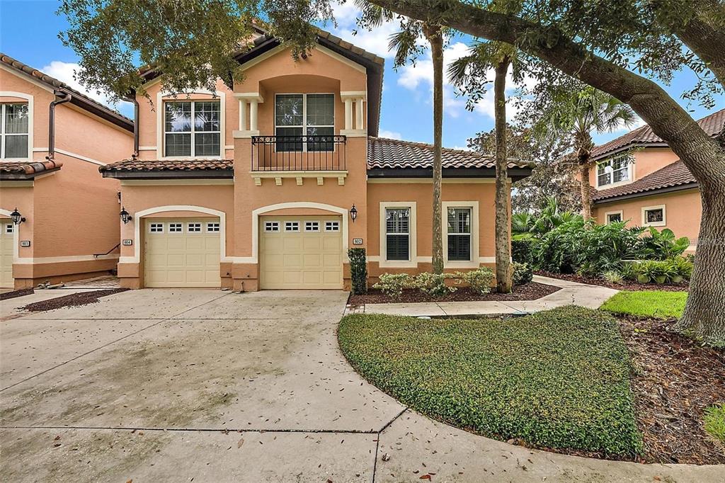 A two-story tan stucco townhouse features two garage doors, a balcony, and a landscaped yard — 802 CAMINO REAL BOULEVARD UNIT 802, HOWEY IN THE HILLS, FL