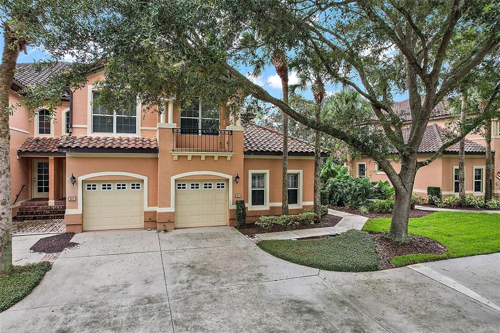 A two-story peach-colored house with a two-car garage and a balcony under large trees — 802 CAMINO REAL BOULEVARD UNIT 802, HOWEY IN THE HILLS, FL