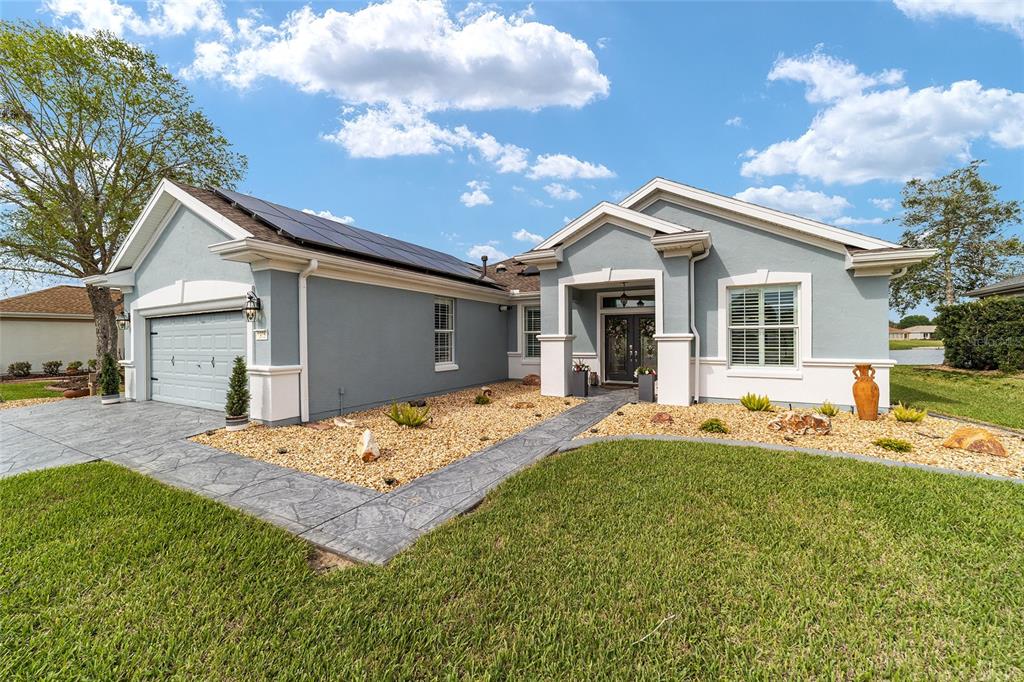 A light blue single-story house with a garage, solar panels, and a stone-patterned walkway — 9375 SE 125TH STREET, SUMMERFIELD, FL