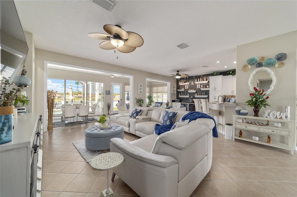 A bright living room features a white sectional sofa, a blue ottoman, and an open kitchen — 9375 SE 125TH STREET, SUMMERFIELD, FL