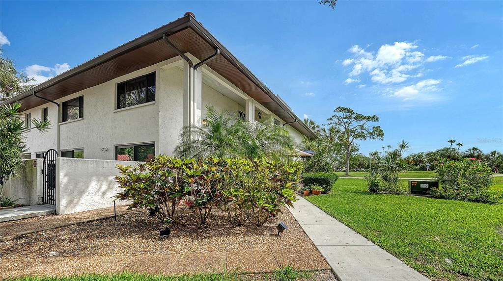 A two-story white stucco building with a brown roof sits beside a grassy lawn — 3500 EL CONQUISTADOR PARKWAY UNIT 148, BRADENTON, FL