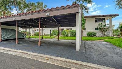 A covered carport structure stands in front of a multi-story residential building with landscaping — 3500 EL CONQUISTADOR PARKWAY UNIT 148, BRADENTON, FL