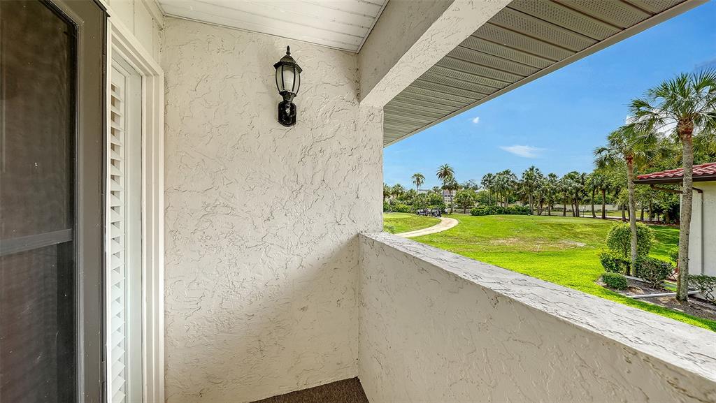 A covered balcony with a textured wall, a light fixture, and a view of greenery — 3500 EL CONQUISTADOR PARKWAY UNIT 148, BRADENTON, FL